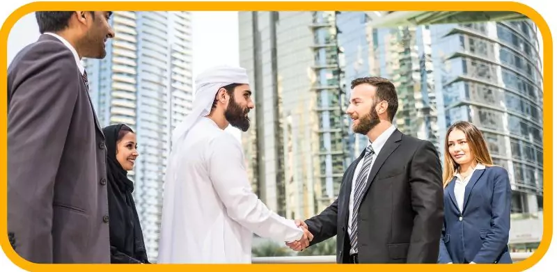 Business professionals, including an Emirati man, shaking hands with skyscrapers in the background.