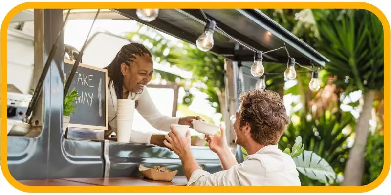 A food truck employee serving a smiling customer outdoors.